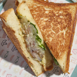 Seandwich pastrami di Ricciola, emulsione di miele e aneto, cetriolini in carpione e insalata Lollo